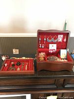 Open vintage wood jewelry box lined with red crushed velvet containing assorted costume jewelry including earrings, brooches, pins, and rings.