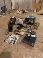 Photo shows vintage phones, adding machine, projector, and bath spa boxes arranged on floor with linens and walls behind.