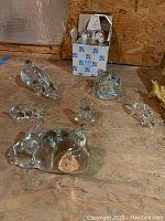 Seven clear glass animal figurines arranged on wooden surface with one boxed item featuring mirror and small glass figures.