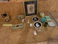Wide shot showing all items including ancient Greek plates with stand, Egyptian framed art, duck figurines, metal tissue box cover, tin bowl, and other ceramics.
