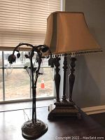 Photo of two table lamps by a window: left lamp with metal leaves and bulbs, right lamp with fabric lampshade and pedestal base