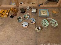 Overview of all ceramic plates, saucers, decorative bread plates, bee-themed plates, soup cup, and candle toppers on wooden surface