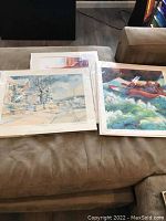 Three signed art prints on couch, two by Magae Hartzell and one by Charles L. Peterson, all sleeved.
