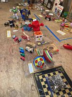 Wide view of assorted toy collection laid out on wooden floor including Buzz Lightyear, Star Wars items, Elmo plush, and various wooden toys.