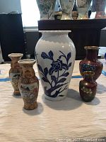 Five Asian vases on floor display including a large white and blue vase, two tall patterned vases, and two small red vases with gold accents.