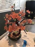 Front side view showing pink jade flowers and green jade berries on slender dark branches positioned in a green jade base with white stones.