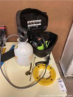 Photo showing Poulan chainsaw in black carrying case with sprayer and wire snake on table.