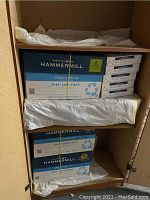 Photo of Hammermill Great White 30 recycled copy paper cases and reams stacked inside a cabinet.
