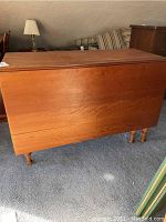 Full side view of wooden drop-leaf cherry dining table with closed leaves showing wood grain and finish.