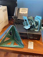 Photo showing Magnavox and Phillips VHS players, Toshiba DVD player, Cisco office phone, and metal and plastic bookends on a wooden surface.