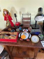 Full view of home decor items on a wooden surface showing clocks, paperweights, tissue box, lamps, and figurine