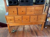 Front view of wooden chest of drawers with 9 drawers, displaying two-tier stepped design and wood grain.