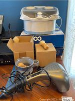 Photo showing three hand-thrown ceramic shaving mugs with wooden-handled brushes, Homedics PA-100 massager, Conair Waterfall Foot Spa model boxes visible below the foot spa unit.