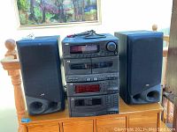 Full view of the stereo system with stacked JVC components and two speakers on either side on a wooden surface.