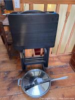 Three black painted wood folding TV tables neatly stacked inside a storage stand with handle, one table face visible.