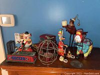 View of all items against blue wall. Items include windup soccer toy, wire metal cage, red duck windup toy, piggy banks, and two vintage metal vehicles.