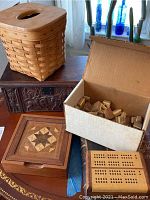 Photo showing Longaberger tissue box holder with wood lid, carved wooden box with scene carving, handcrafted wooden box with geometric inlay, cardboard box with vintage mahjong tiles, and wooden cribbage board.