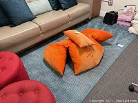 Photo of the blue area rug spread out on floor under couch with orange pillows on top, showing size and condition