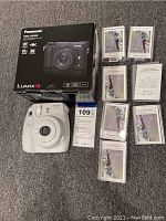 Overview showing Panasonic Lumix G box, Fujifilm instax mini 9 camera, film packs