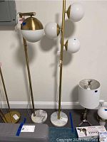 Both floor lamps standing side by side showing their full height, marble bases, and white glass globe shades against a neutral wall background.