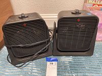 Two black Trustech portable electric heaters side by side showing the front grills, red indicator lights and rotary dial controls on top.