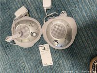 Two off-white, circular Homedics white noise machines shown from the front, with speaker grills, control knobs, and power cords on blue carpet.