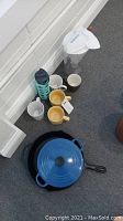 Lot shows a blue Le Creuset Dutch oven with lid, a black cast iron skillet, several mugs and a Soma pitcher.