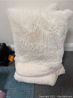 Two cream-colored sherpa style pillows standing upright on a folded sherpa blanket.
