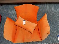 Photo showing entire orange seat cushion with attached armrest padding and matching throw pillow placed on top. Cushion and pillow show dirt and discoloration.