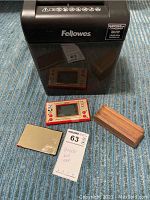 Black Fellowes paper shredder with slot and Nintendo Mickey Mouse handheld game on carpet.