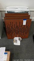 8 wood acoustic panels stacked vertically with mounting hardware and instruction sheet on floor in front