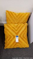 Pair of two yellow throw pillows, one showing the front textured chevron pattern and the other showing the back smooth side with DKNY label