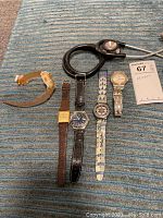 Five wristwatches laid out horizontally with a black stethoscope above them on a blue textured surface