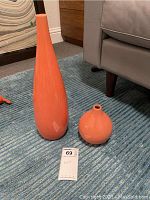 Pair of orange vases on carpet, one tall slender and one short round, with West Elm labels visible on the underside.