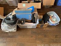 Photo of multiple plastic bins and boxes on the floor containing various electronics, batteries, cords, and household items in no particular order.