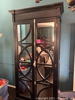 Front view of the tall black armoire cabinet showing mirrored double doors with geometric circular wood overlay.