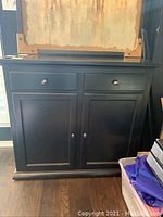 Front view of the black cabinet showing two drawers above and two doors below, with round knobs.