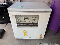 Front view of white chest freezer with Javita Weight Loss Coffee advertisement on front panel, showing some wear and yellow ribbon sticker.