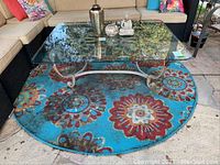 Glass top metal base coffee table placed on round mandala patterned outdoor rug.