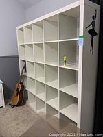 Full view of large white cube organizer shelving unit next to a guitar and wall decal, showing its size and grid of cubbies.