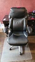 Black padded office chair with armrests and caster wheels in front of desk.