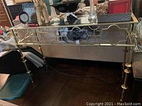 Full view of the metal table featuring smoke glass top and brass enamelled decorative metal legs and frame with geometric design.