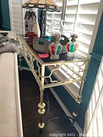 Full side view showing smoke glass top, brass-colored enamel metal base with geometric design, and metal legs with footrest.
