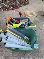The plastic tubs contain various rolled papers, plastic bats, toys and books stacked together outside.