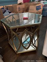 Full view of the hexagonal table showing the glass top, brass geometric base, and glass bottom shelf