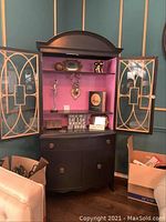 Full front view of the wooden hutch showing the break front glass doors open revealing bright pink interior back panel and shelving. Lower section shows drawer and cabinets closed. Various objects inside and around are excluded from the sale.