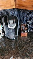 Photo showing Keurig coffee maker with clear cup and wooden knife block with knives