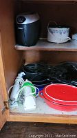 Cupboard shelf with ice cream maker, slow cooker, electric griddle, red ceramic baking dishes