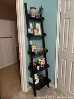Full view of the black leaning ladder shelf with five shelves, leaning against a wall, shown with decorative objects but contents not included.