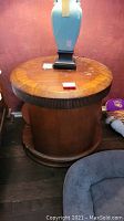 Round wooden nightstand with fluted trim and visible scratches on top surface, lamp on top